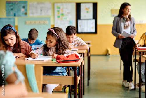 Hispanic schoolgirl and her classmates writing in classroom.