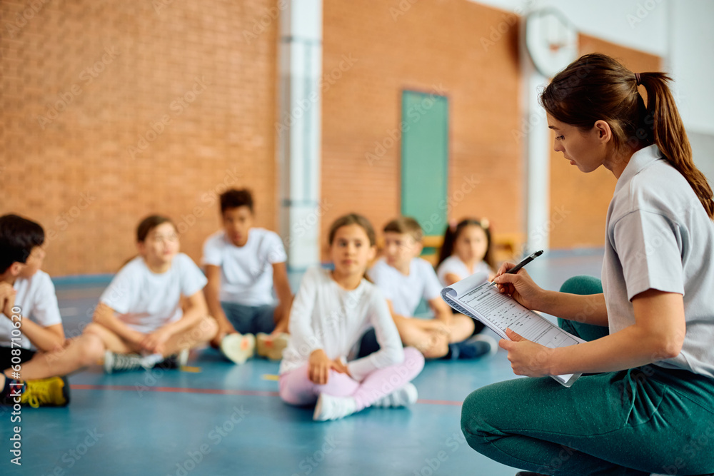 Physical education teacher taking notes during class with school kids. Physical education teacher taking notes during class with school kids.