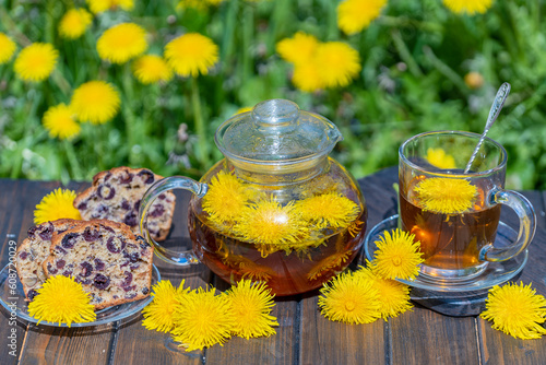 Healthy dandelion flower tea in a glass teapot on the wooden table in the spring garden, closeup