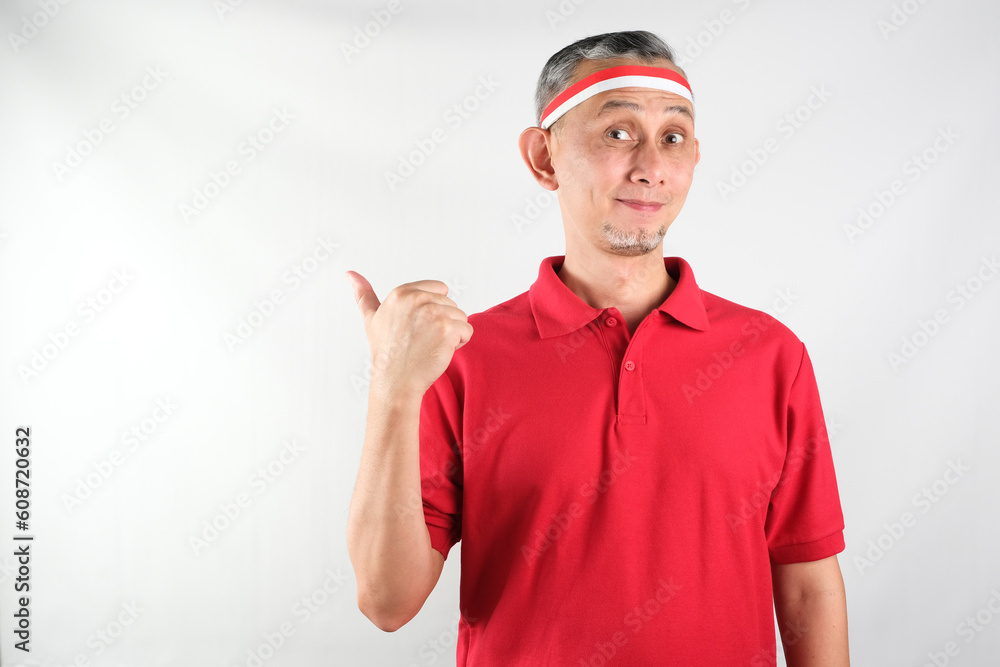 Portrait of Asian Man wearing red and white Indonesia flag attribute looks happy doing positive gesture with thumbs up, smiling
