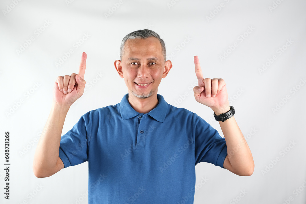 Asian man wearing tshirt pointing fingers up at copy space isolated over white background.
Asian man wearing tshirt pointing fingers up at copy space isolated over white background.