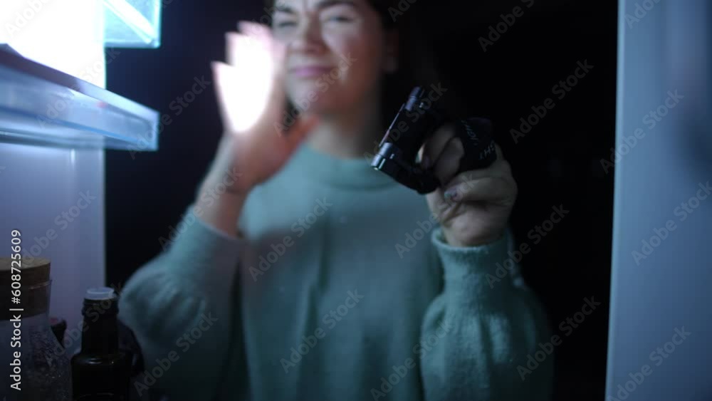 View from fridge young woman with flashlight making disgust facial expression smelling bad odor closing door. Caucasian lady in darkness with spoiled food in refrigerator during blackout View from fridge young woman with flashlight making disgust facial expression smelling bad odor closing door. Caucasian lady in darkness with spoiled food in refrigerator during blackout