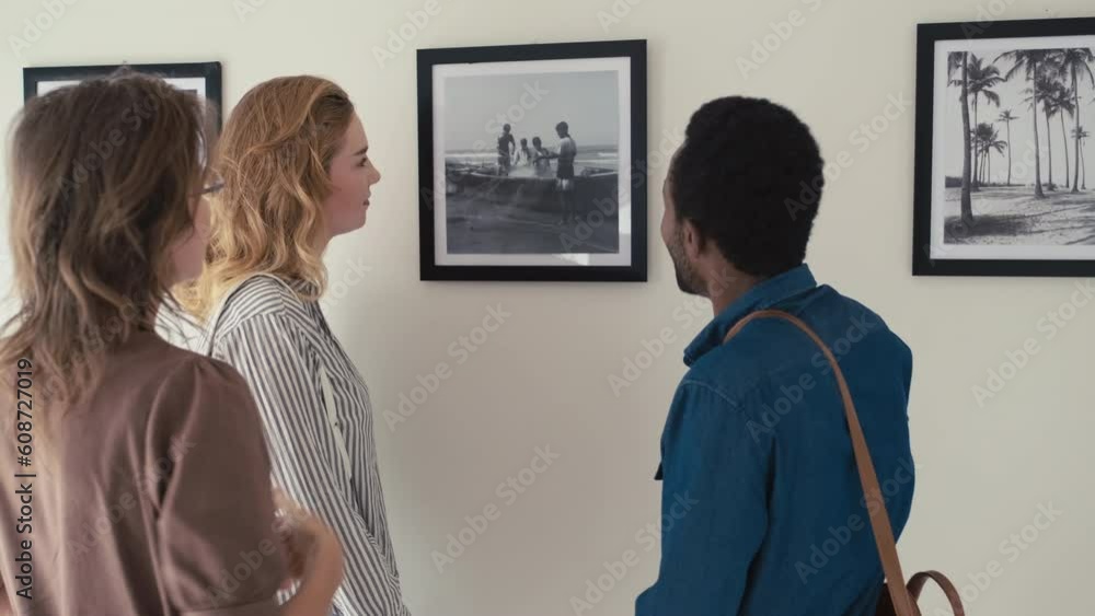 Medium shot of group of multi-ethnic male and female visitors discussing artwork on photo exhibition in gallery Medium shot of group of multi-ethnic male and female visitors discussing artwork on photo exhibition in gallery