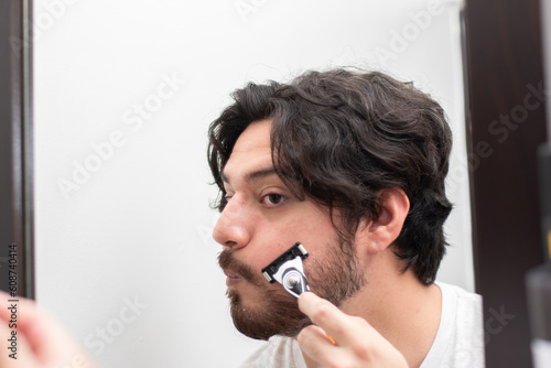 Person looking himself in mirror while he is shaving his beard with copy space