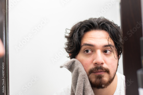 Young man drying face with towel front mirror with copy space