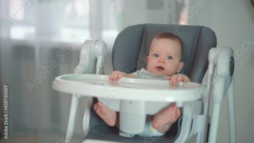 Cute baby boy of ten-months old sitting in a baby chairand smiles. Concept of the first complementary food photo