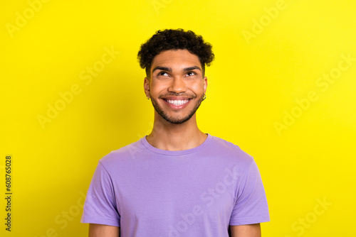 Photo of positive thoughtful guy dressed purple t-shirt looking up empty space isolated yellow color background