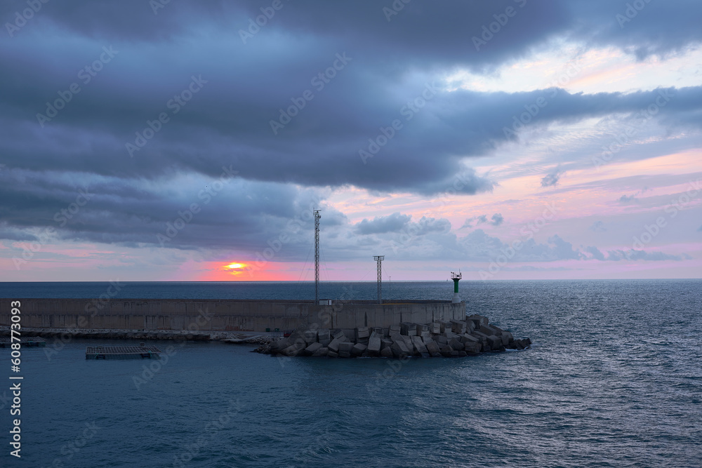Sunrise from green lighthouse on maritime breakwater