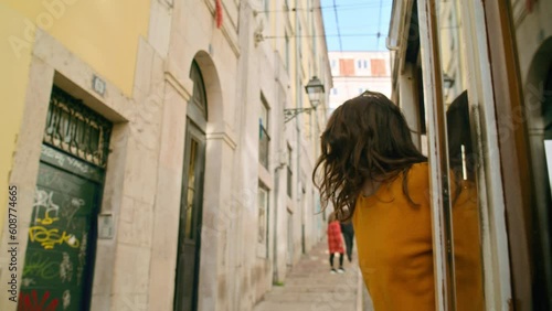 Beautiful and authentic millennial young woman lean out of window of old tram in Lisbon, Portugal city centre. Concept amazing european summer vacation, wanderlust trip in cinematic urban destination