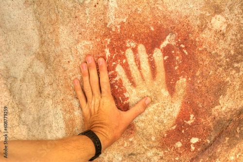 Photo of a hand touching a rock with a hand print in Cueva de las Manos, Argentina
