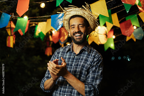 A lively man in a straw hat and vibrant attire, dancing with enthusiasm amidst the joyful Brazilian June festival - Festa Junina photo