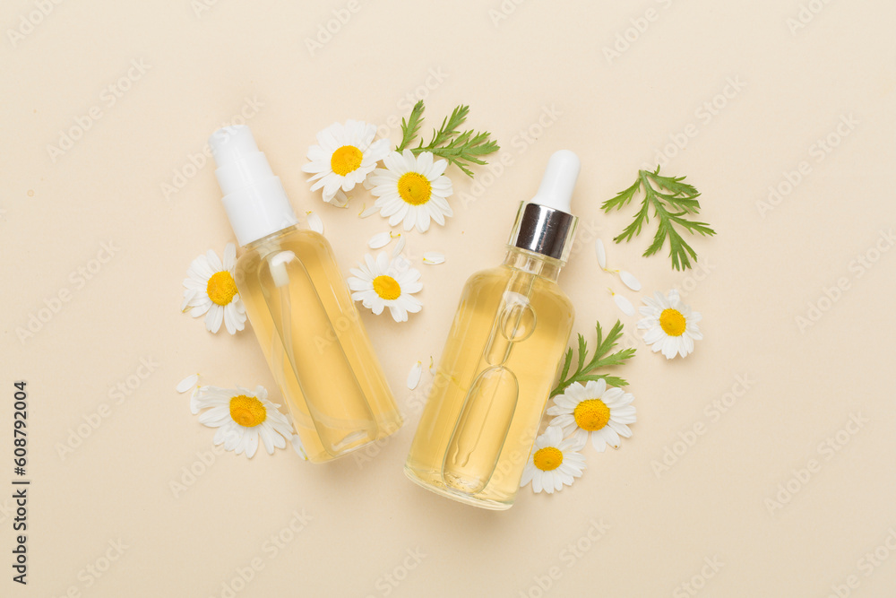 Bottles with chamomile essential oil and flowers on color background, top view Bottles with chamomile essential oil and flowers on color background, top view