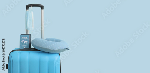 Packed suitcase with passports, medical mask and pillow on light blue background with space for text