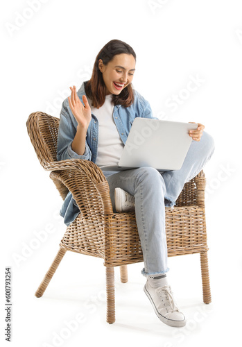 Young woman using laptop in wicker armchair on white background