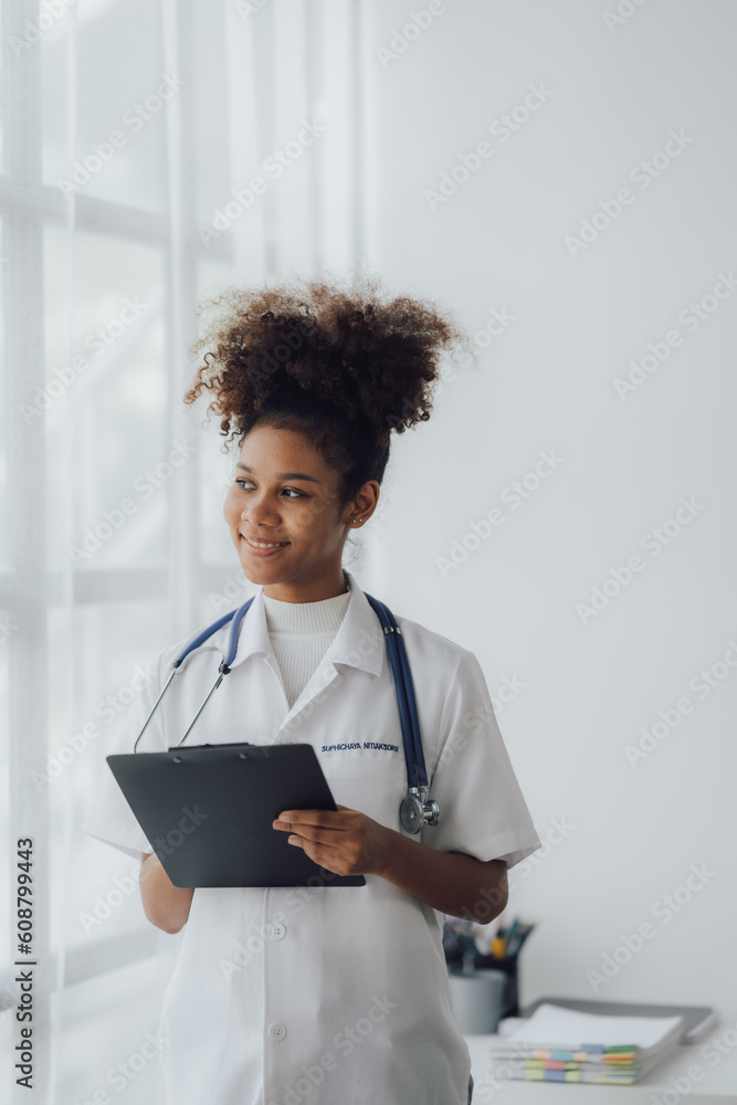 Young African american female doctor using smartphone and working with computer while sitting at the clinic room. Young African american female doctor using smartphone and working with computer while sitting at the clinic room.