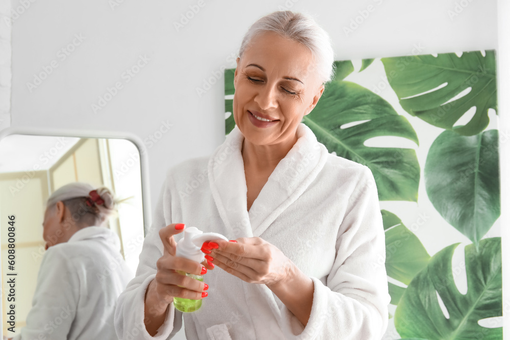 Mature woman applying cosmetic product with cotton pad in bathroom Mature woman applying cosmetic product with cotton pad in bathroom