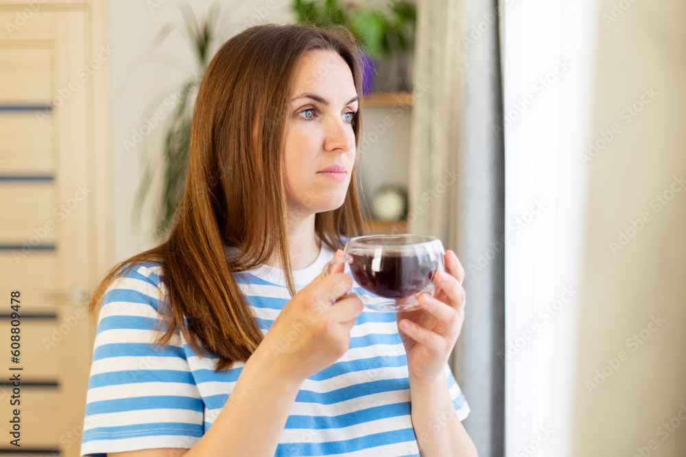 A beautiful young woman drinking tea near the window of the house A beautiful young woman drinking tea near the window of the house