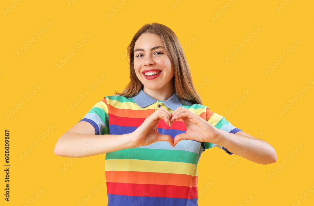 Young woman in rainbow shirt making heart with hands on yellow background Young woman in rainbow shirt making heart with hands on yellow background