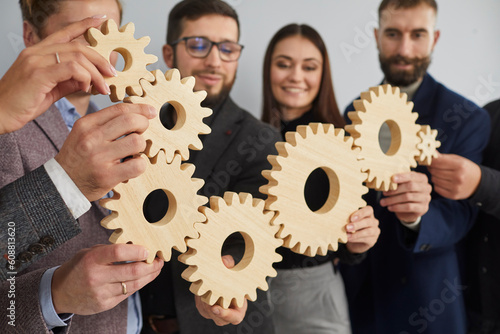 Smiling happy business colleagues assembled figure of gears. Close-up of seven wooden gears, which was assembled by friends and colleagues into single mechanism. Successful productive teamwork concept
