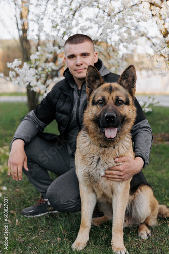 a handsome man in the spring near a blooming plum tree with a shepherd dog. with a dog in the spring garden, family spring photo. dog is man's friend