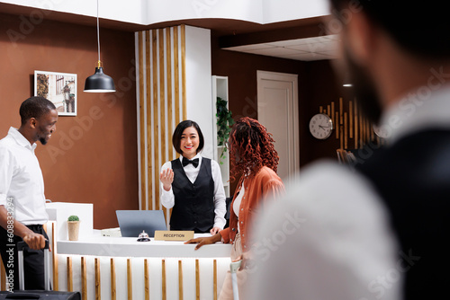 Foto Receptionist talking to hotel guests at front desk counter in lobby, giving advice about luxury room service