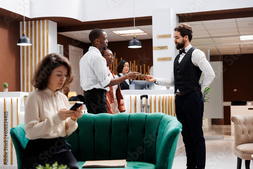 Hotel concierge taking cash from man, accepting to carry suitcases and help with bags after registration at front desk. Young adult working as porter at luxury resort, receiving money tip.