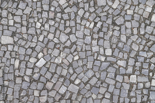 Texture of an old stoneblock pavement cobbled with gray stone tiles of different shapes as a background