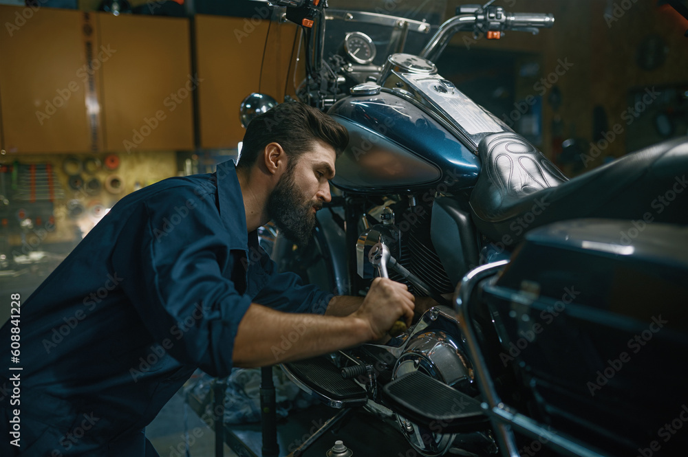 Man repairing motorcycle using wrench while working at repair workshop Man repairing motorcycle using wrench while working at repair workshop