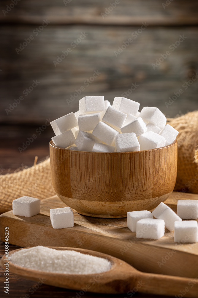 White sugar cubes in wooden bowl and granulated sugar on wooden spoon. White sugar cubes in wooden bowl and granulated sugar on wooden spoon.