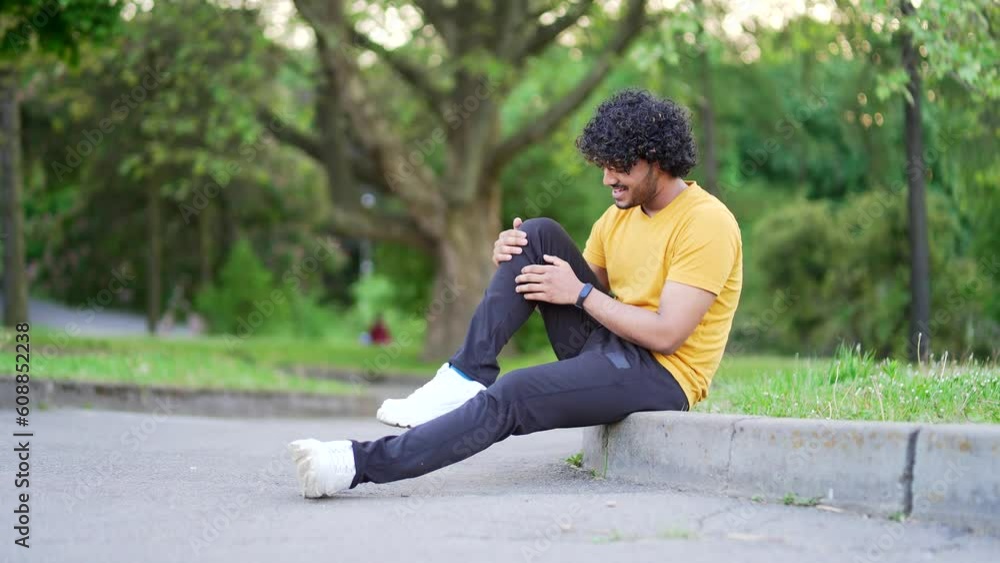 Young athlete runner sitting with muscle pain in city park. Man