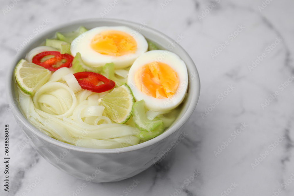 Bowl of delicious rice noodle soup with celery and egg on white marble table, closeup. Space for text Bowl of delicious rice noodle soup with celery and egg on white marble table, closeup. Space for text