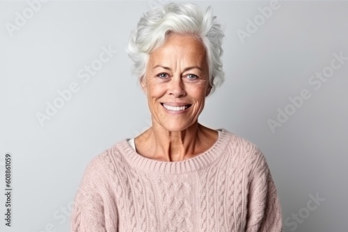 Portrait of a happy senior woman smiling at the camera while standing against grey background