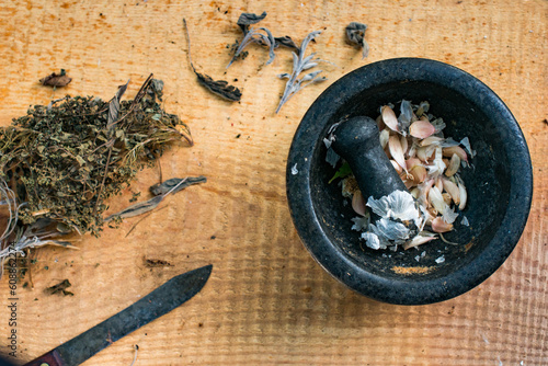herbs, a garlic filled black molcajete and a rustic knife on a wood board photo