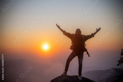 Young man hiker on a top of a mountain standing on top of cliff in summer mountains at sunset and enjoying view of nature