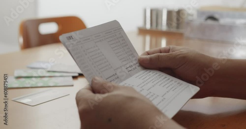 Hands opening bank book to check balance on wooden table
