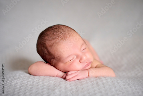 A naked newborn sleeping on her hands on top of a gray blanket