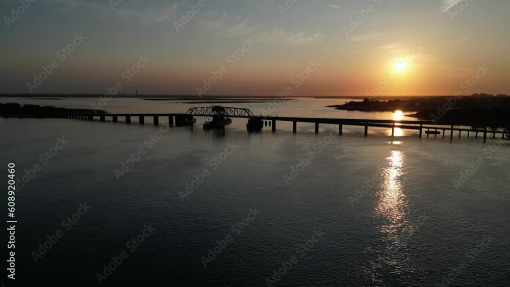 An aerial view of the Jamaica Bay, facing the sun at sunrise. A train bridge is view as the sun reflects onto the calm waters below. The drone camera truck right and pan left over the water. An aerial view of the Jamaica Bay, facing the sun at sunrise. A train bridge is view as the sun reflects onto the calm waters below. The drone camera truck right and pan left over the water.