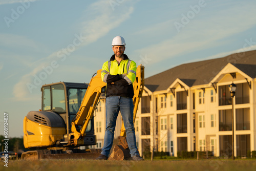 Builder in a construction site. Builder with excavator ready to build new house. Construction builder wear building uniform on excavation truck digging, builder with buildings construction background.