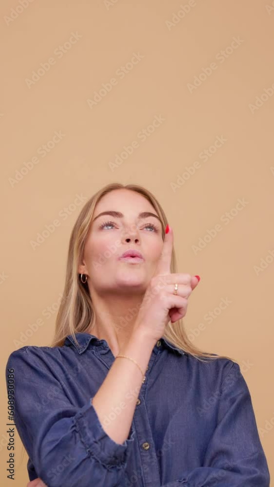 Beautiful young woman thinking and wondering pointing upwards at your logo or text, copyspace Beautiful young woman thinking and wondering pointing upwards at your logo or text, copyspace