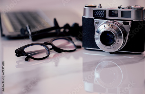 Closeup, desk and photography studio with camera, glasses and computer for art, journalist or news company. Retro equipment, spectacles and professional lens with laptop in office for newspaper job
