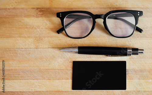 Glasses, pen and notebook on a desk in empty office for abstract background, business and vision. Eye sight, ideas and planner or journal on wooden table for reading and creative writing mockup space