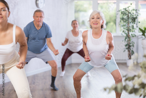 Elderly woman engaged in fitness. In dance hall of studio, she learns to perform active movements of modern youth hip hop