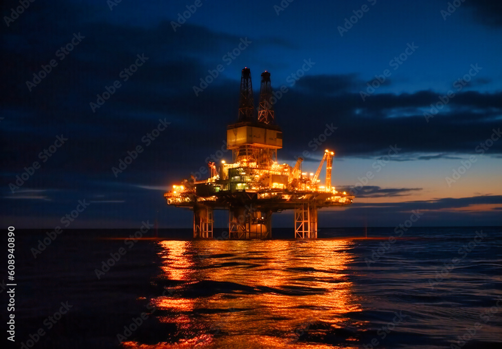 an oil rig that is illuminated at dusk floating offshore