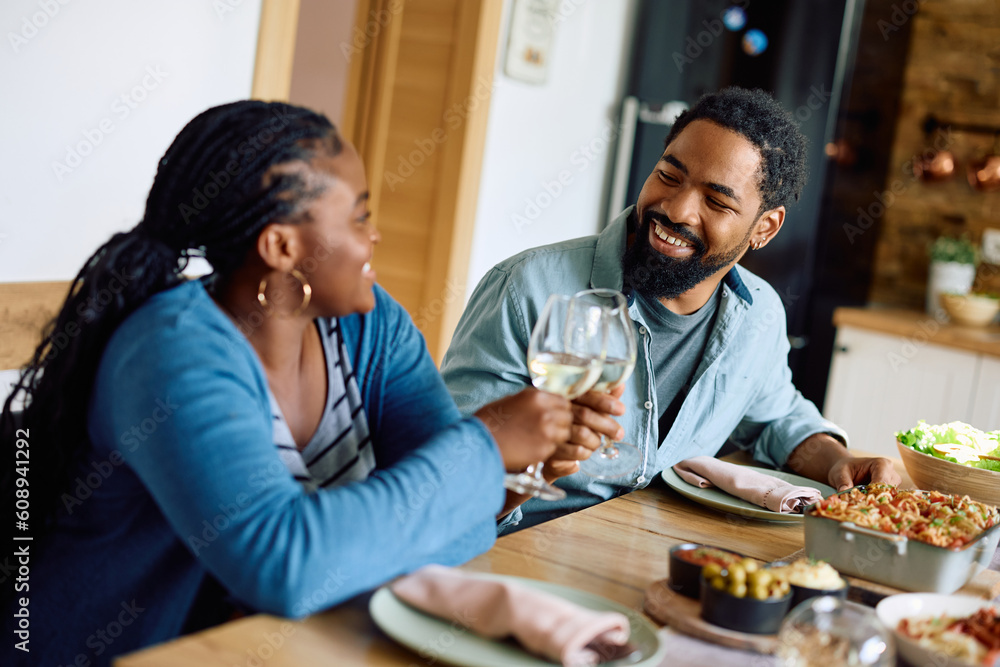 Happy black man and his wife toast with wineglasses while eating at dining table