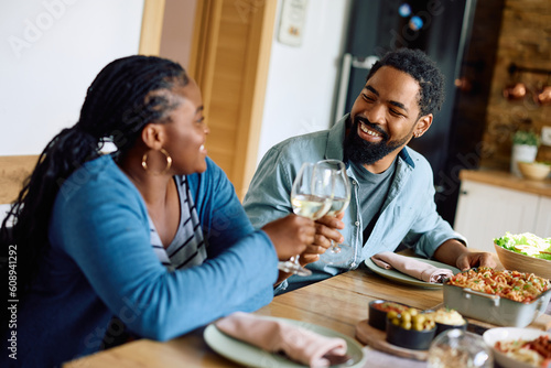 Happy black man and his wife toast with wineglasses while eating at dining table