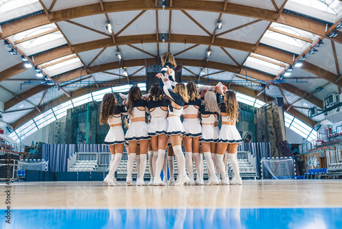 Cheerleaders female team practicing, holding a girl in the air on the basketball court. High quality photo