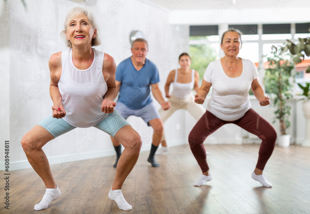 Group of happy mature sports women and man in activewear exercising dynamic dancing movemens in modern gym studio