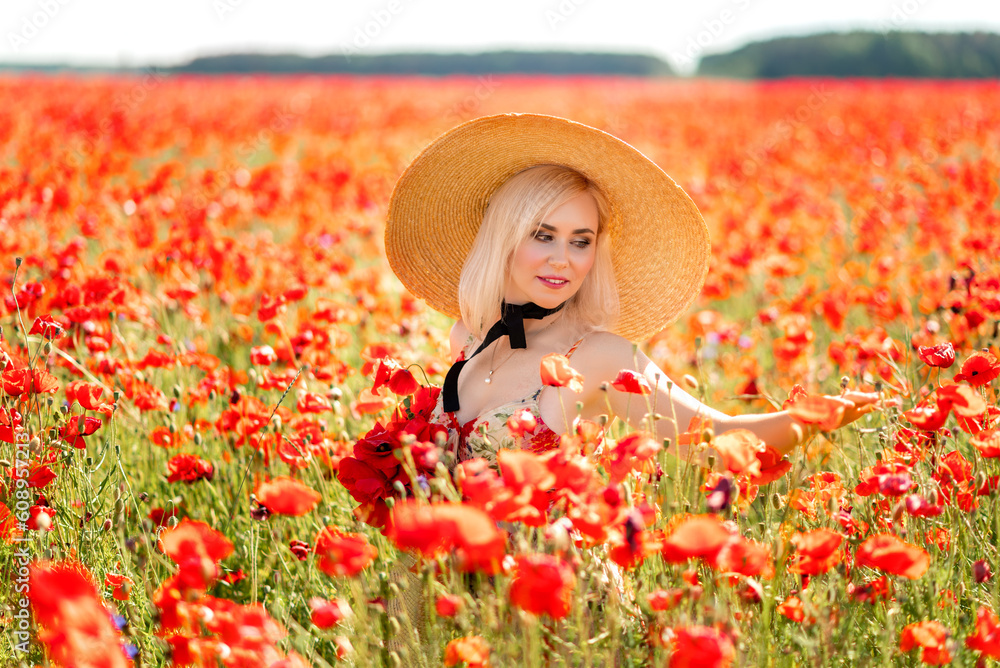 Summer portrait of a blonde woman in a poppy field. A girl with a big hat and a bouquet of red flowers