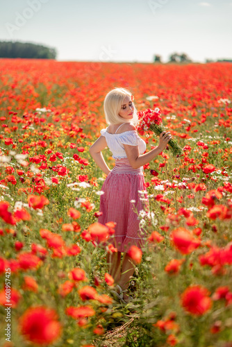 blonde woman walks in a poppy field collecting a bouquet of flowers