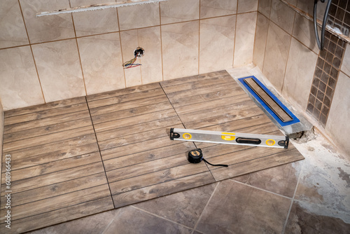 Linear floor level shower. Wood effect ceramic tile and modern metallic linear drain installation in the bathroom
